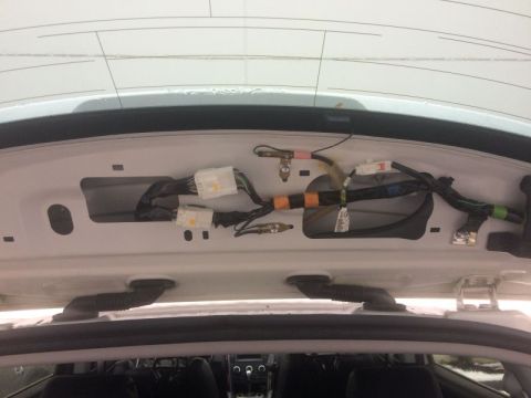 2009 Mazda CX-9 - The interior of a white vehicle's rear hatch area shows exposed wiring harnesses and connectors attached to the body panel above the rear w…