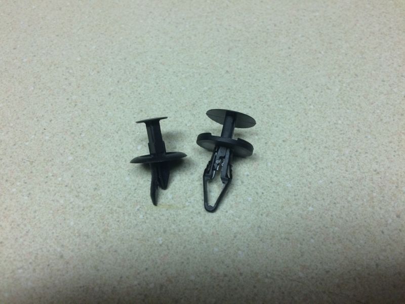 Two black plastic automotive clips on a speckled surface