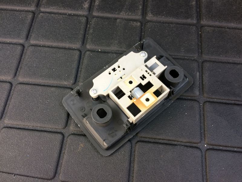 Disassembled interior light fixture with black base and beige/white internal components on a black textured surface.