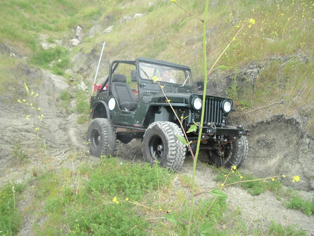 Dark green open-top Jeep on lifted off-road tires parked on a dirt embankment
