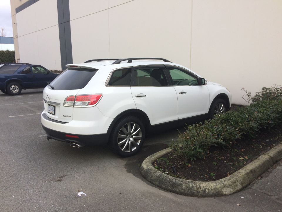 White 2009 Mazda CX-9 parked next to a building with a blue SUV in the background.