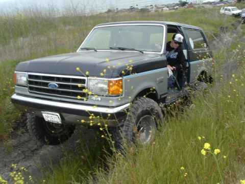 1989 Ford Bronco - This Ford Bronco is navigating a grassy, off-road trail with a driver and passenger visible.