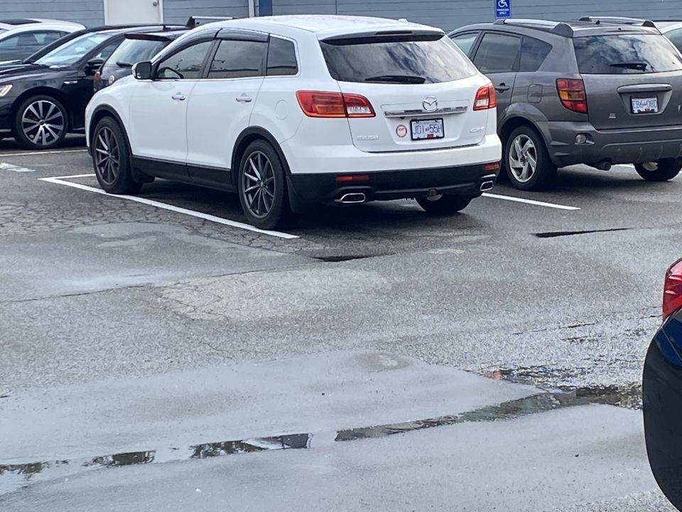 White Mazda CX-9 parked in a wet parking lot next to a dark gray Pontiac Vibe.