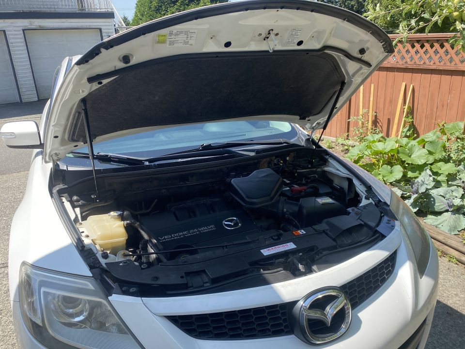 White 2009 Mazda CX-9 with hood open, showing V6 engine and coolant reservoir.