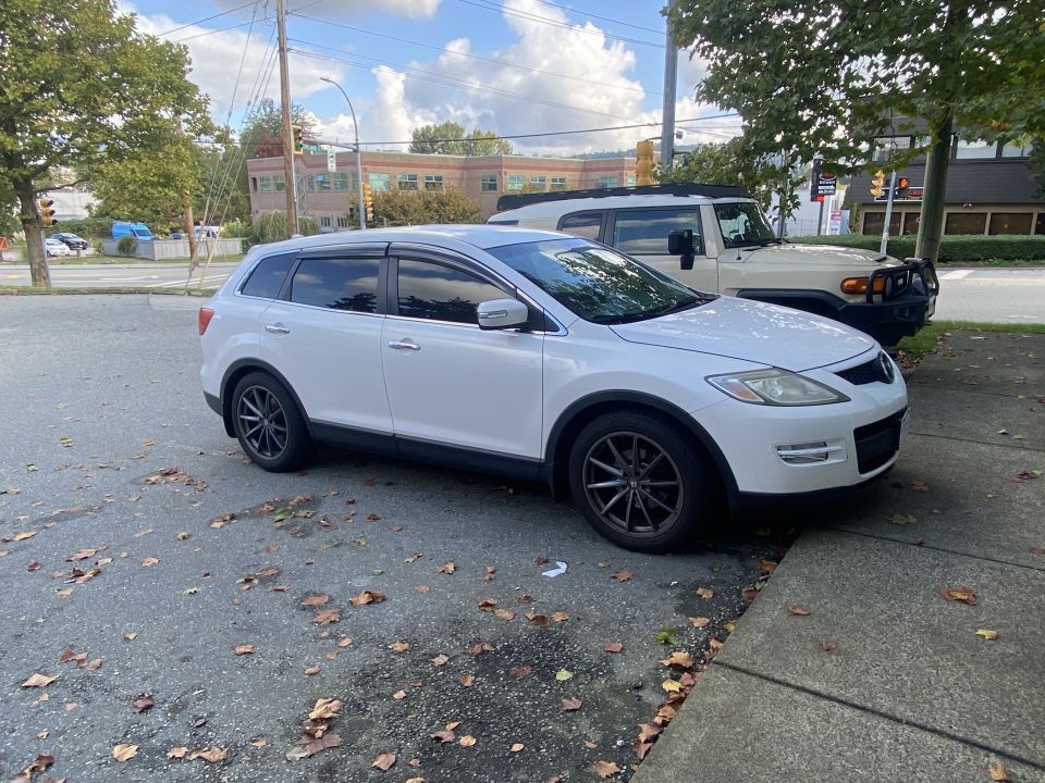 White 2009 Mazda CX-9 with dark gray wheels parked next to a tan Toyota FJ Cruiser.