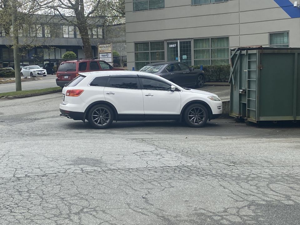 Side view of a white 2009 Mazda CX-9 SUV parked next to a green dumpster.