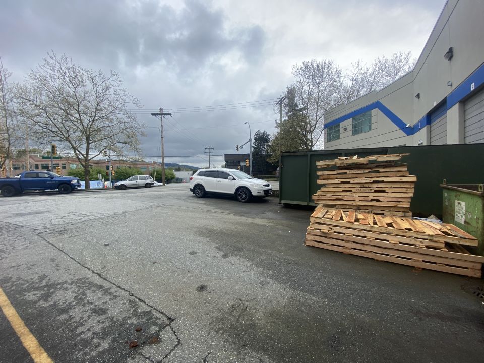 White 2009 Mazda CX-9 parked on wet asphalt lot next to pallets and dumpster.