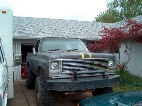 1979 Ford Bronco - A heavily modified pickup truck is parked in front of a garage, with another vehicle partially visible.