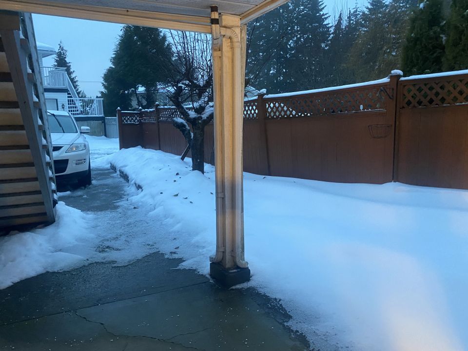 White SUV parked in a snowy driveway next to a house and fence.