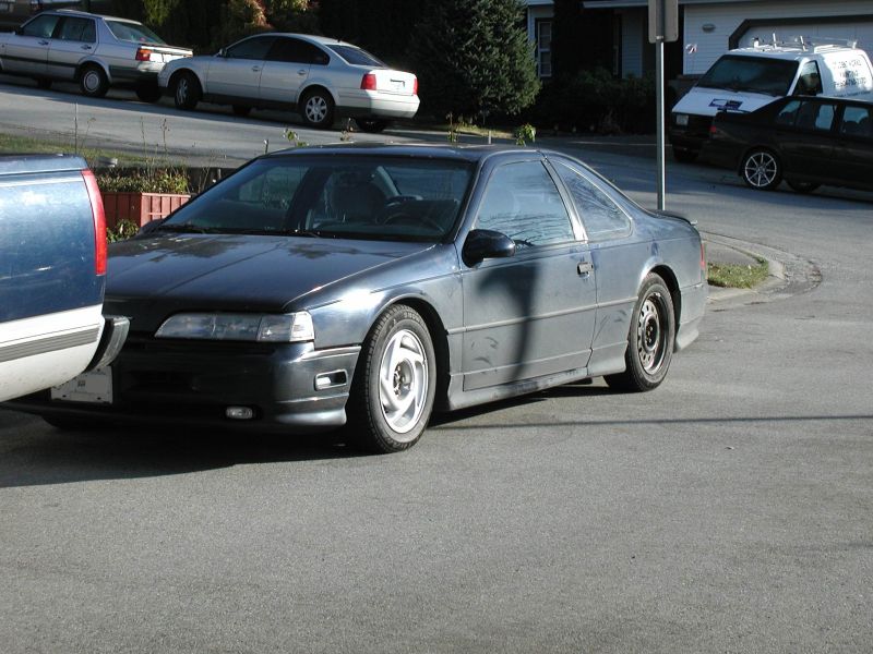1990 Ford Thunderbird coupe, dark gray, parked on asphalt driveway, front 3/4 view.