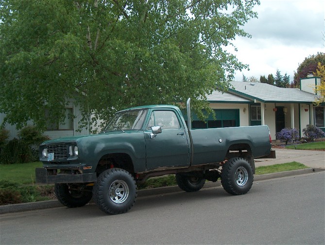 Green lifted pickup truck parked on a residential street. Exhaust stack visible behind the cab