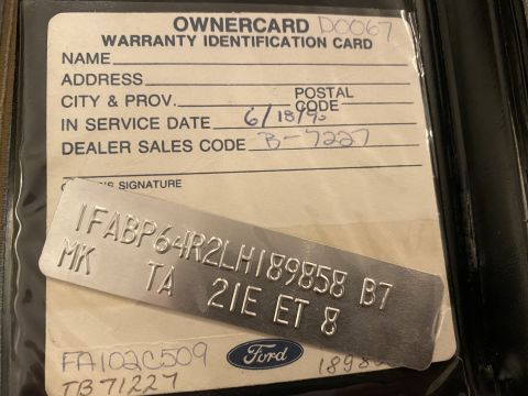 1990 Ford Thunderbird - A close-up shot of a 1990 Ford Thunderbird owner's warranty identification card with a metal VIN plate resting on top. The card has handwri…