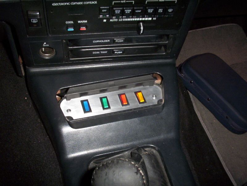 Custom switch panel with blue, green, red, and yellow illuminated switches in a car's center console.