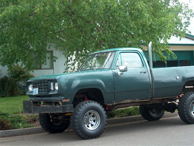 Green lifted pickup truck with large tires and side exhaust pipe parked in front of a house