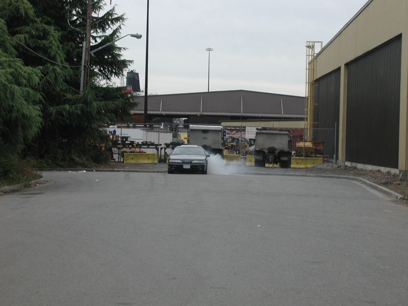 Dark sedan drifting and smoking tires in an industrial area.