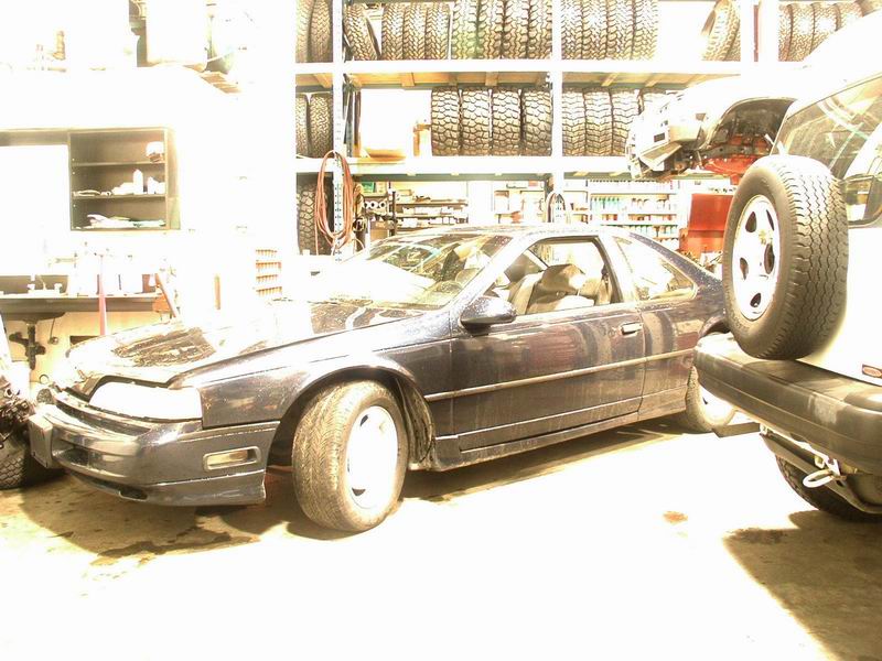 1990 Ford Thunderbird coupe in a garage with tires on shelves.