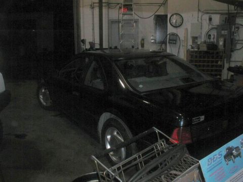 1990 Ford Thunderbird - The rear driver's side of a black 1990 Ford Thunderbird is visible in a garage setting. The car has a sunroof and a badge that reads "Super…