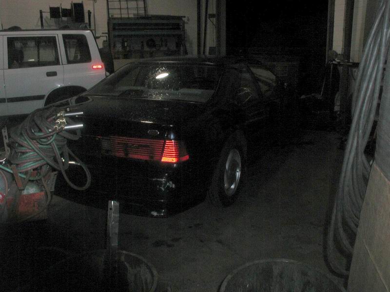 Rear passenger side of a black coupe in a garage, next to a white SUV.
