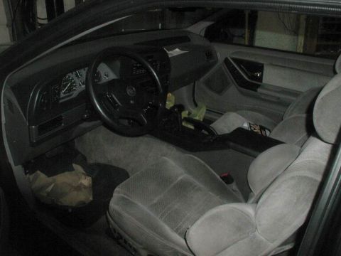 1990 Ford Thunderbird - The interior of a Ford Thunderbird is shown, featuring grey fabric seats, a black dashboard with gauges, and a black steering wheel. A cent…
