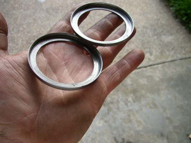 Two metal axle seals held in an open palm over a concrete driveway