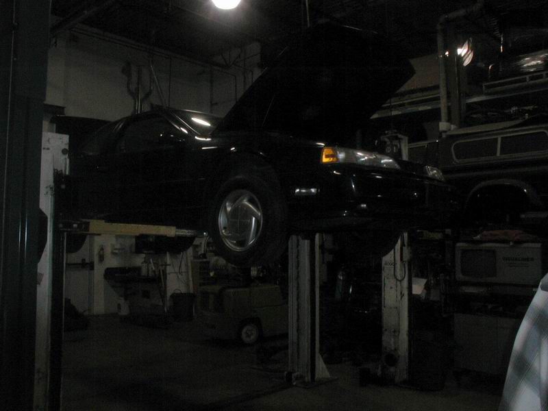 Black coupe on a car lift with hood open in a garage.
