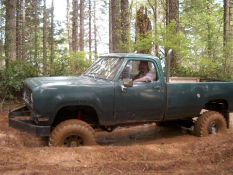 1979 Ford Bronco - A man drives a lifted green pickup truck through a muddy forest trail.