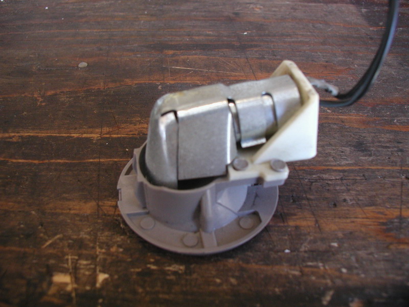 Gray and silver electrical socket with black wires on a wooden surface.