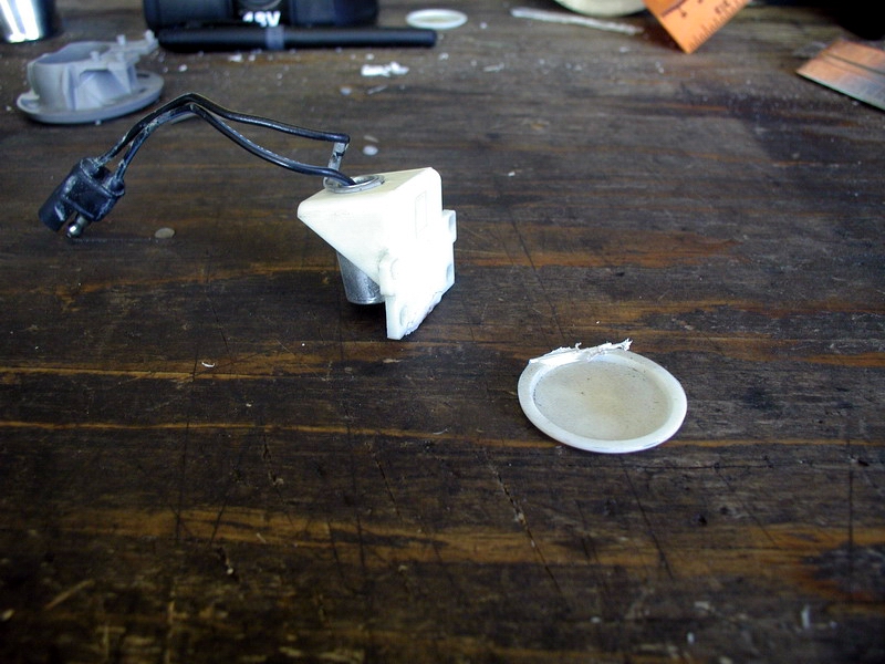 White plastic electrical connector with wires and a detached circular part on a wooden table.