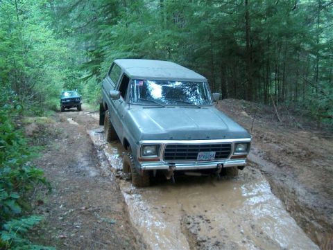 1979 Ford Bronco - A gray 1978 Ford Bronco navigates a muddy trail in a forest, with another vehicle following behind.