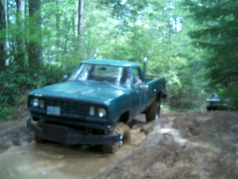 1979 Ford Bronco - A green pickup truck navigates a muddy trail in a wooded area, with another vehicle visible ahead.