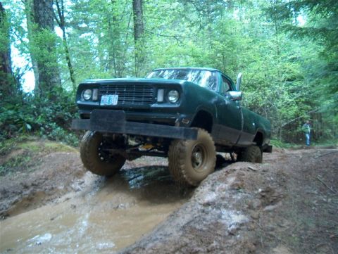 1979 Ford Bronco - Pickup truck navigates a muddy off-road trail in a wooded area.