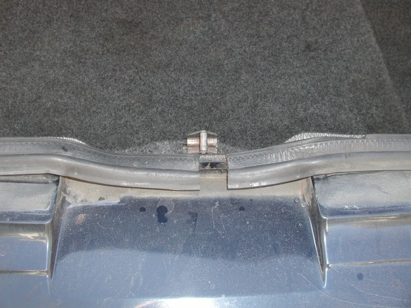 Close-up of a car trunk hinge and rubber seal.