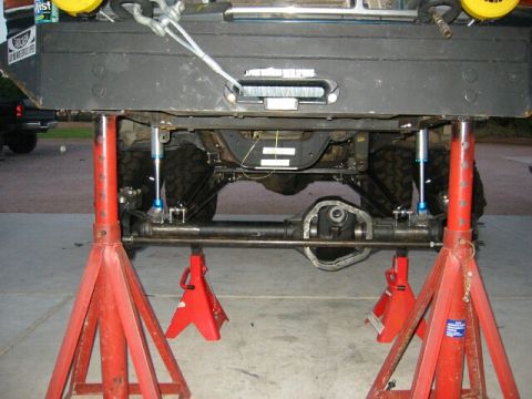 1994 Ford Bronco - The underside of a vehicle is elevated on red jack stands, revealing the suspension components and rear differential.