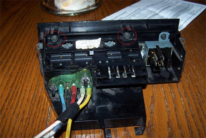Automotive electrical component with wires attached and screws circled.