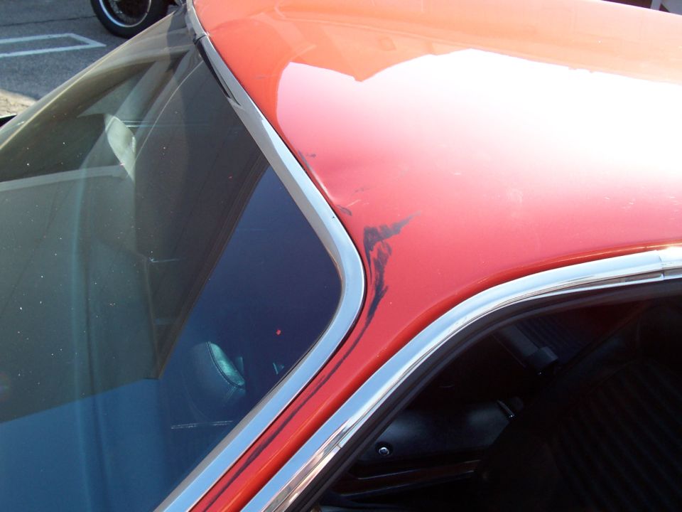 Orange coupe C-pillar with chrome trim and paint scuffs near rear window