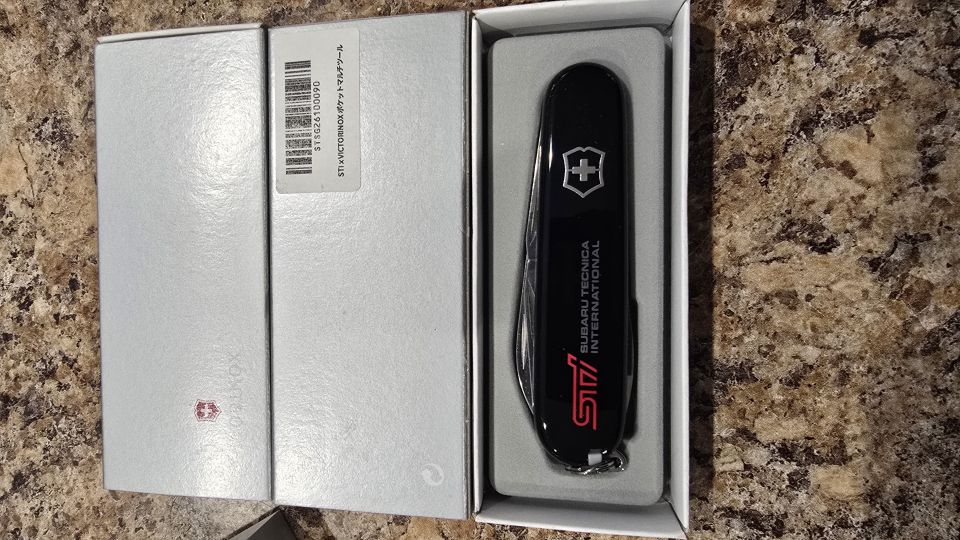Closed black STI Victorinox pocket knife seated in its open white gift box