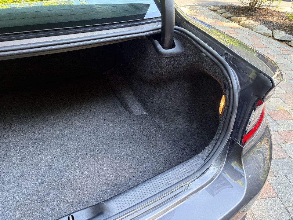 Empty carpeted trunk of dark gray sedan seen from the passenger rear corner