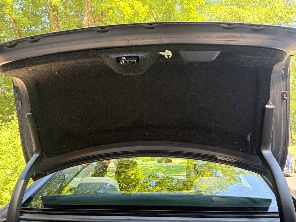 Underside of open sedan trunk lid with carpet liner and glow emergency release handle