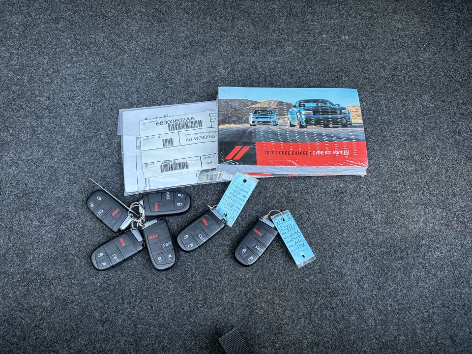 Six Dodge key fobs, 2020 Charger owner's manual and a parts bag on gray carpet