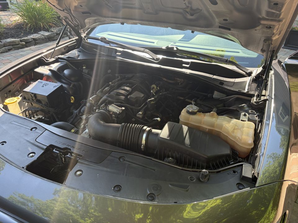 Engine bay of gray sedan with airbox, coolant tank and CHARGER-stamped radiator cover