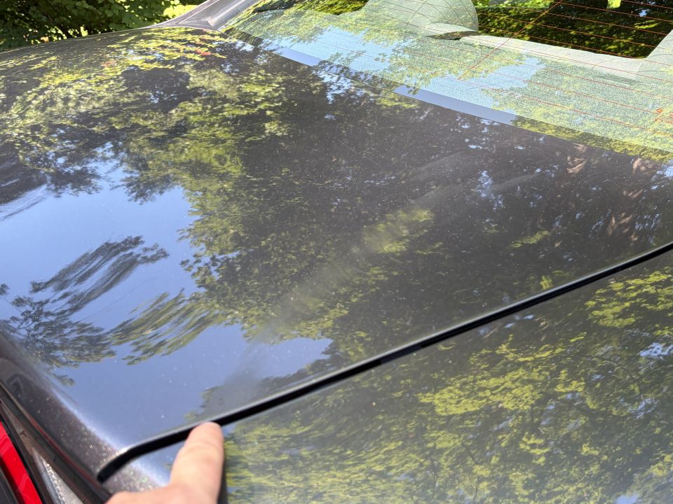 Dark gray sedan trunk lid and rear glass with finger at the panel seam