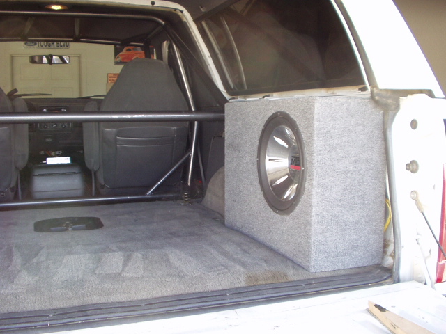 Subwoofer enclosure box mounted in the rear cargo area of an SUV with roll cage