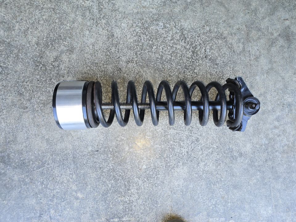 Coilover shock assembly with black coil spring and aluminum canister on concrete floor