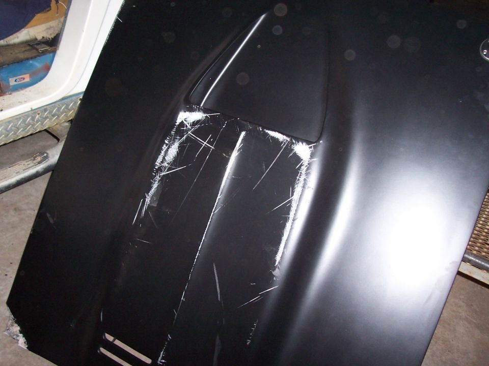 Black hood panel with a scoop and heavy scratches in a workshop