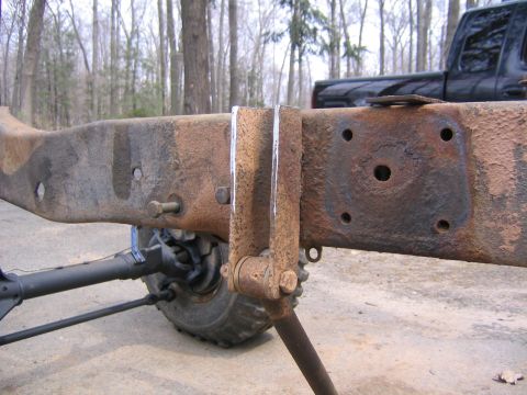 1978 Ford Bronco - Close-up of a stripped, heavily surface-rusted truck frame rail on a bare rolling chassis, with a fabricated bracket bolted through the rai…