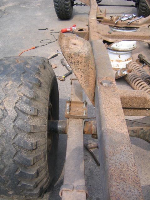 1978 Ford Bronco - Close overhead look down a stripped, heavily surface-rusted truck frame rail during disassembly, showing the rear leaf spring, shackle and…