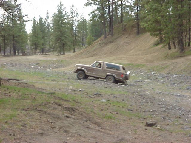 Brown Ford Bronco driving on a rocky, wooded trail