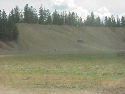 1989 Ford Bronco - An off-road vehicle navigates a steep dirt incline, with a line of trees bordering the top of the hill.