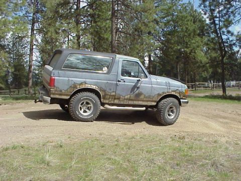 1989 Ford Bronco - This Ford Bronco is parked outdoors on a dirt road, with trees and a fence visible in the background.