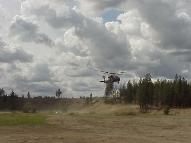 Helicopter flying over a dirt field with trees and clouds. Supermotors.net logo visible